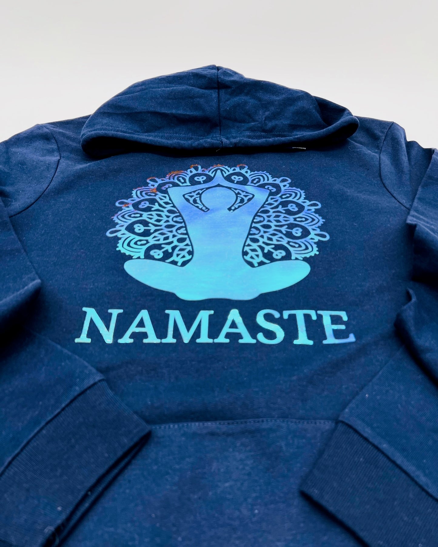 Bild einer Yoga-Position mit Blume des Lebens und der Unterschrift "Namaste" in Hologramm Flexfolie. Je nach Lichteinfall aendert sich die Farbe und erzielt einen 3D-Effekt.