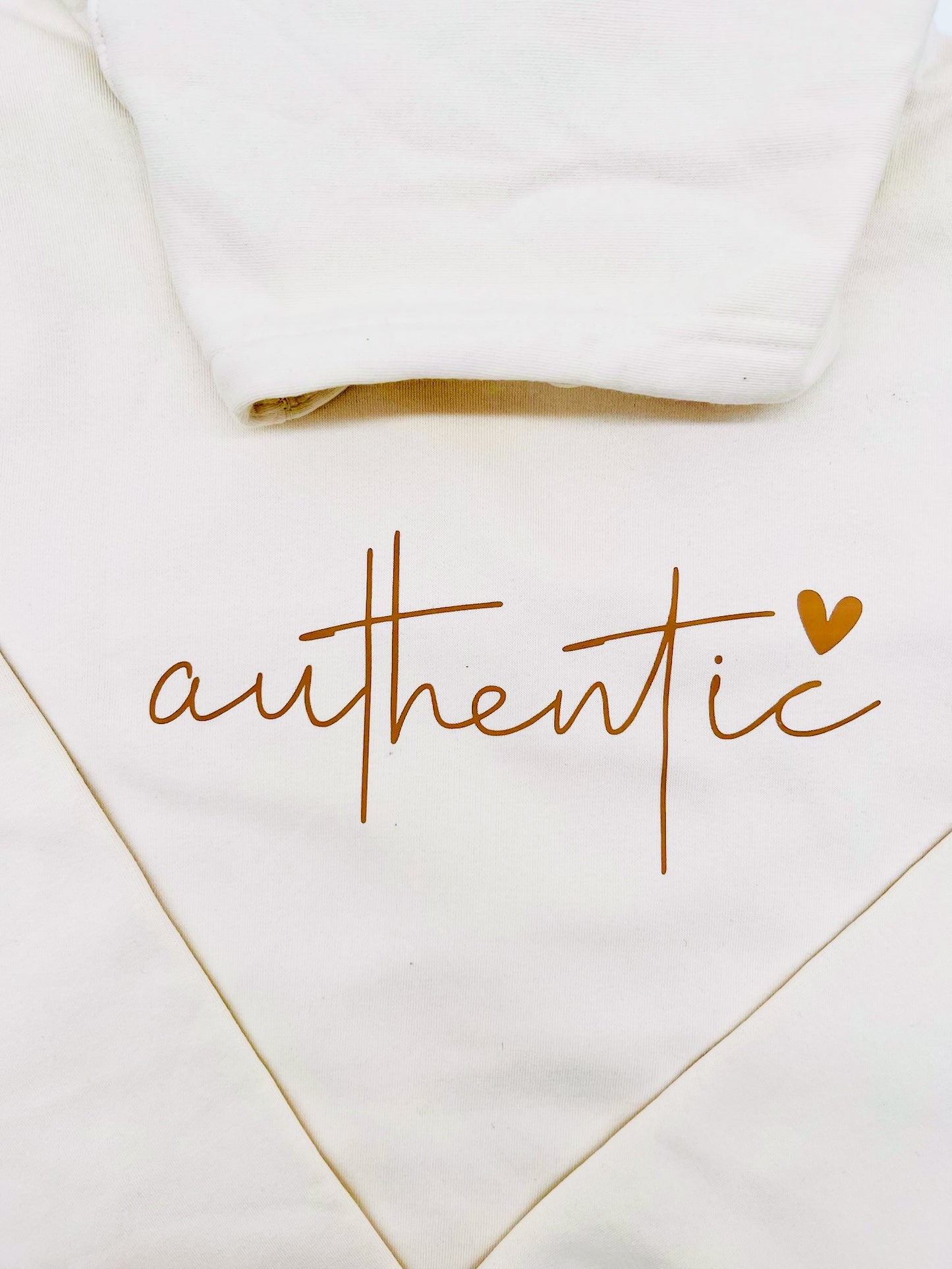 Hoodie in creme farbe. Das Bild zeigt im Detail das, in einem Brauchton, auf der Brust gedruckte Wort "authentic". Ueber dem Buchstaben "c" ist ein Herz abgebildet.
