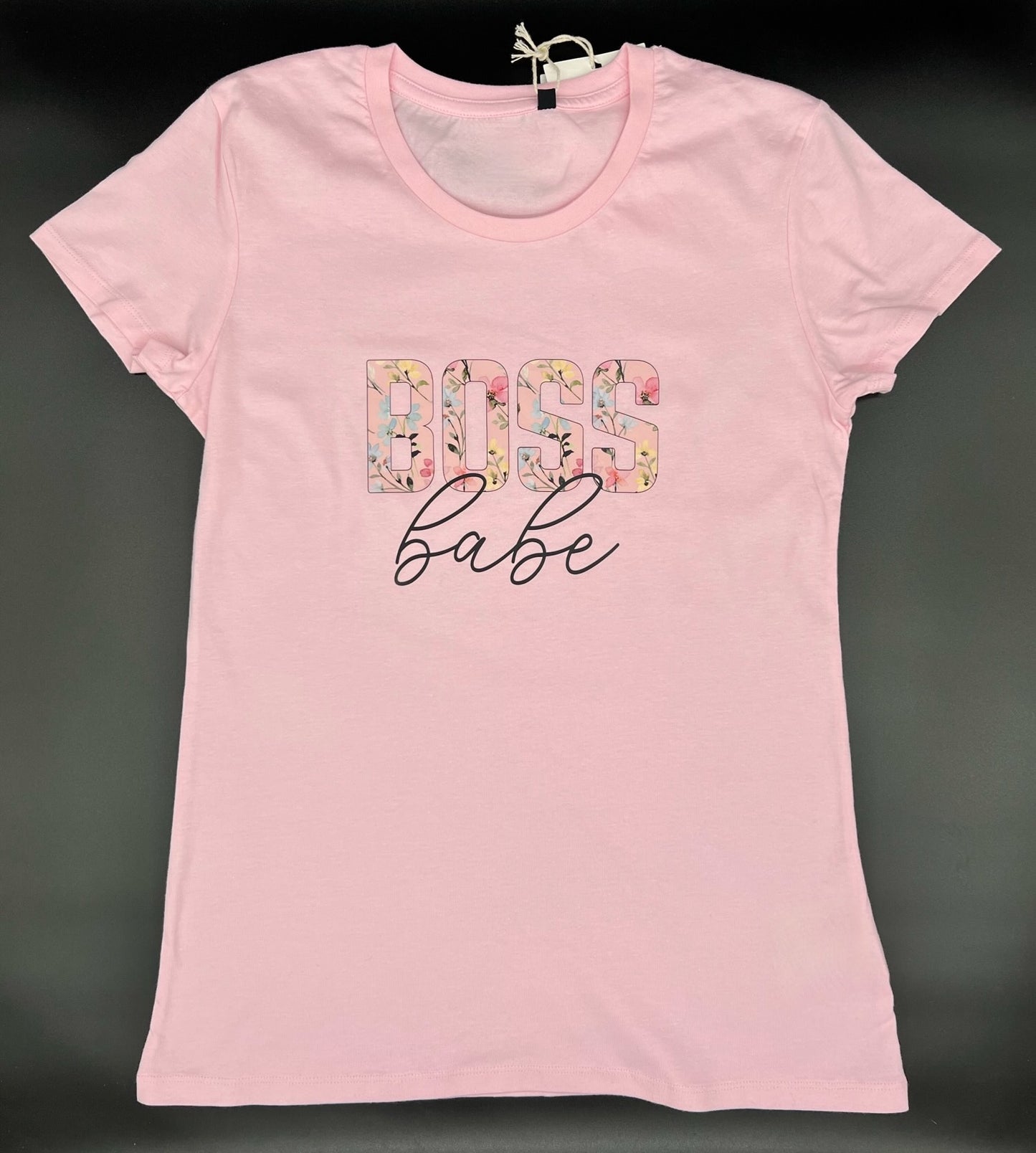 Damen T-Shirt in hellrosa. Auf der Brust ist der Aufdruck "BOSS babe". Das Wort "BOSS" ist in Blockschrift und die einzelnen Buchstaben sind mit Blumen und Blueten in gelb, hellblau und rosa abgebildet. Das Wort "babe" steht darunter kursiv in schwarz geschrieben.