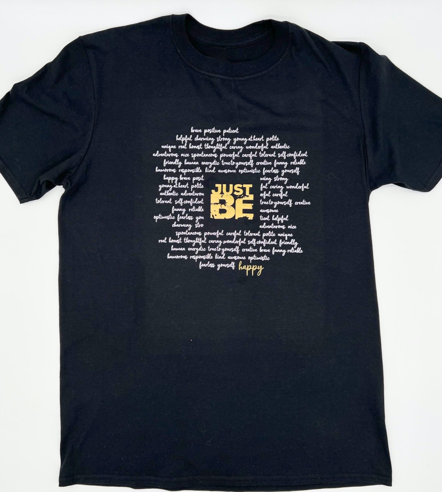 T-Shirt in schwarz. Ueber die gesamt Brust sind viele Woerter kursiv in weiss geschrieben die einen Kreis formen. Im Zentrum steht in Blockschrift in gold "JUST BE" und schliesst den Kreis der Woerter unten rechts mit dem Wort "happy" in gold.
