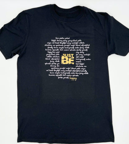 T-Shirt in schwarz. Ueber die gesamt Brust sind viele Woerter kursiv in weiss geschrieben die einen Kreis formen. Im Zentrum steht in Blockschrift in gold "JUST BE" und schliesst den Kreis der Woerter unten rechts mit dem Wort "happy" in gold.