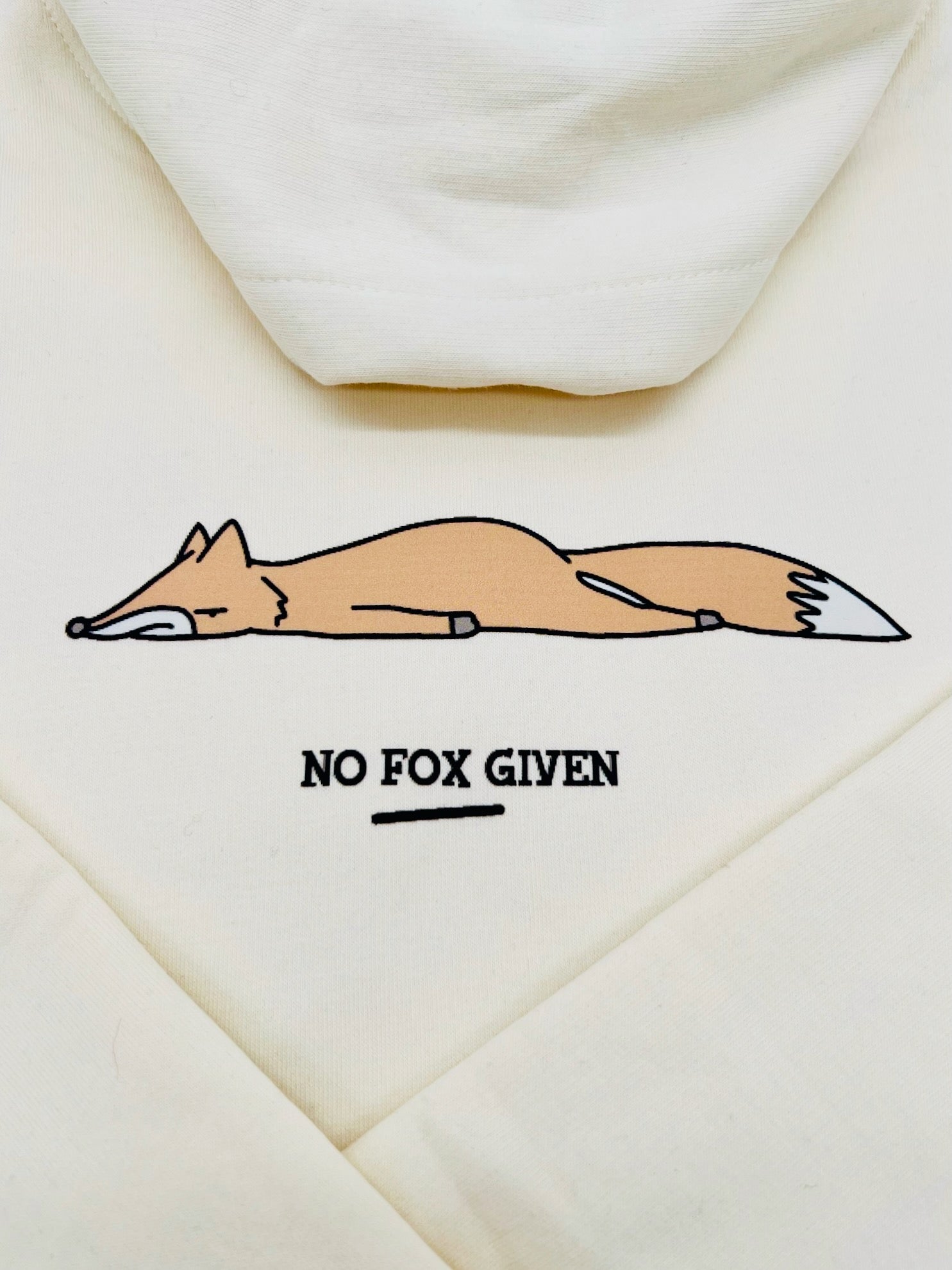 Detailansicht des Aufdrucks. Abgebildet ist ein Fuchs in hell-rot-braun der auf alllen Vieren liegt. Darunter steht "NO FOX GIVEN" mit Unterstreichung in schwarz.